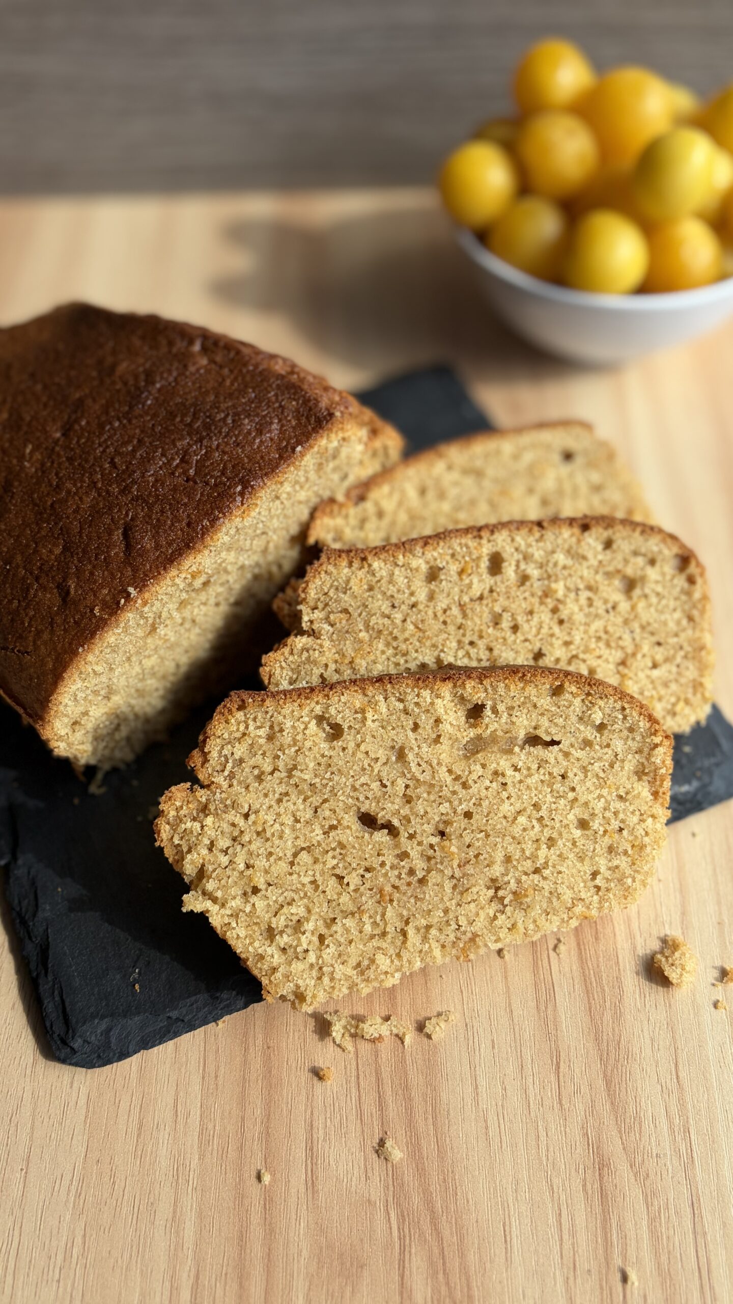 Fette di plumcake alle susine in friggitrice ad aria con susine fresche sullo sfondo.