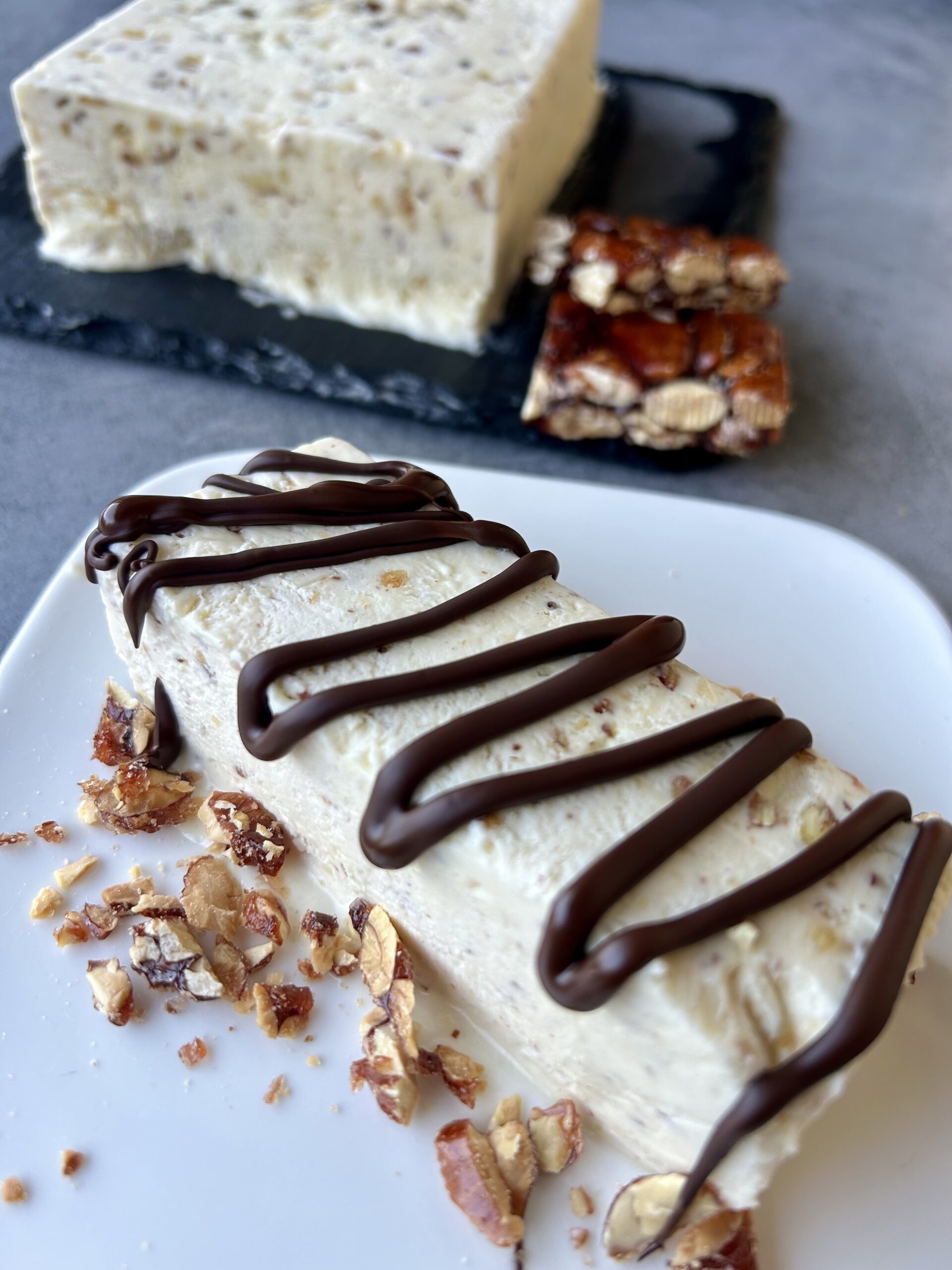 Fetta di semifreddo al croccantino con yogurt greco decorata con cioccolato fondente e croccante alle mandorle
