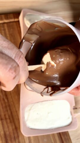 Gelato a stecco immerso in un bicchiere con cioccolato al latte fuso