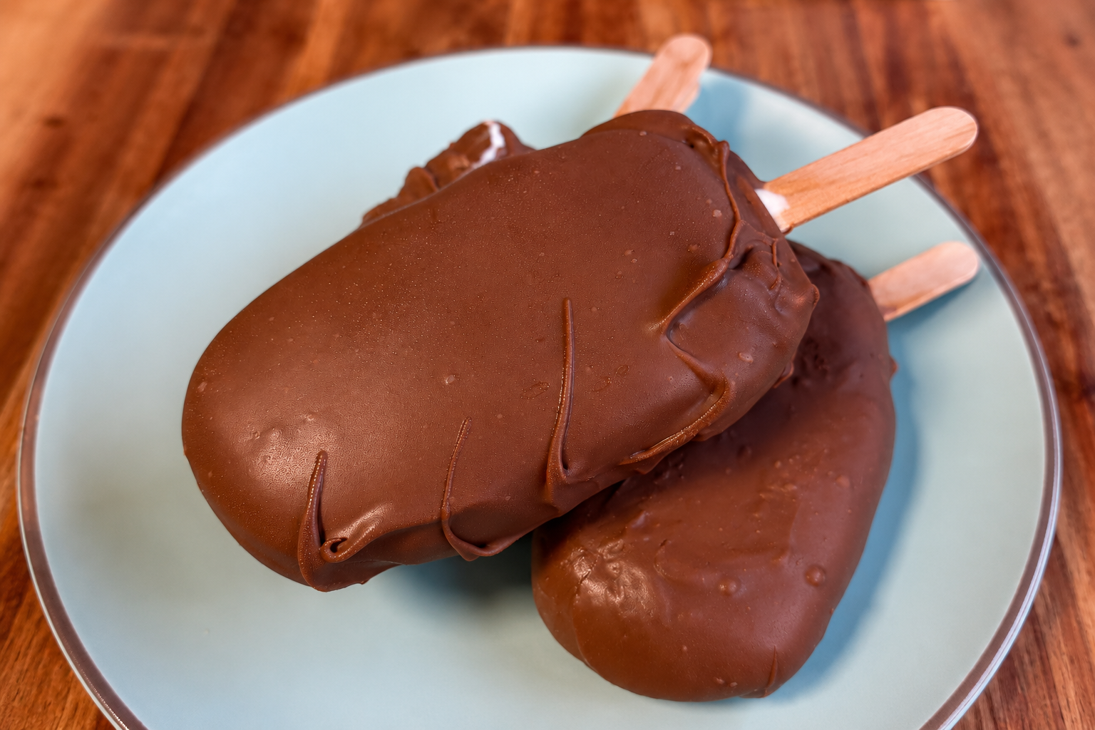 Gelati a stecco con 2 ingredienti ricoperti di cioccolato al latte su un piatto azzurro
