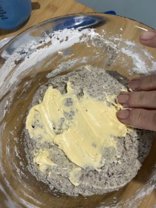 Burro morbido aggiunto all'impasto dei panini al grano saraceno senza glutine in una ciotola di vetro.