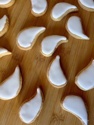 Biscotti fantasma di pasta frolla ricoperti di ghiaccia reale bianca, disposti su un tagliere di legno.
