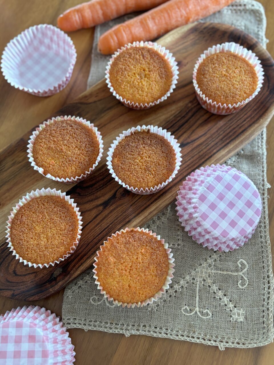 6 muffin soffici alle carote senza glutine su vassoio di legno, sul piano abbelliscono la scena dei pirottini di carta e due carote fresche
