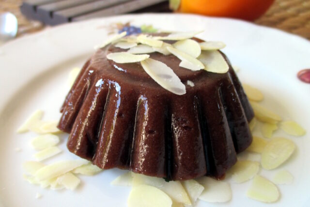 Budino cachi cioccolatoso sformato su un piatto bianco con lamelle di mandorla