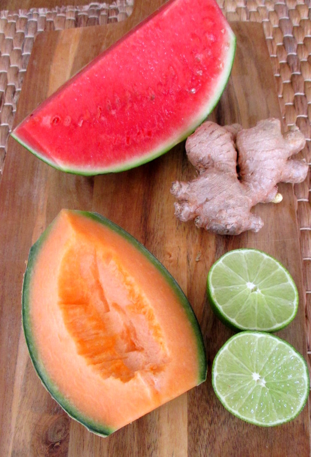 Preparazione bevanda depurativa anguria e melone: fette di frutta fresca, lime tagliato a metà e zenzero intero su un tagliere di legno