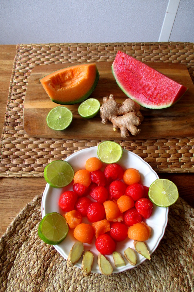 Preparazione bevanda depurativa anguria e melone: polpa di frutta ridotta a palline, fettine di lime e zenzero disposte su un piatto bianco