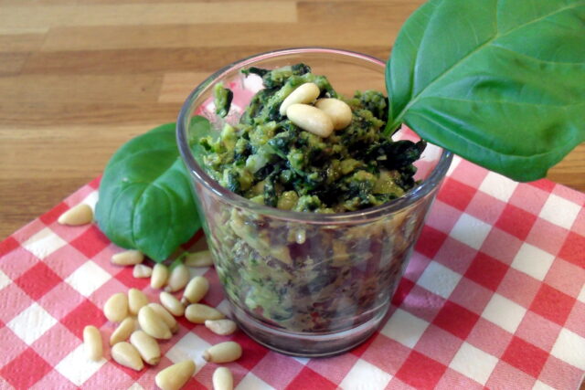 Pesto di basilico light in bicchiere con pinoli sparsi sulla tovaglia a scacchi