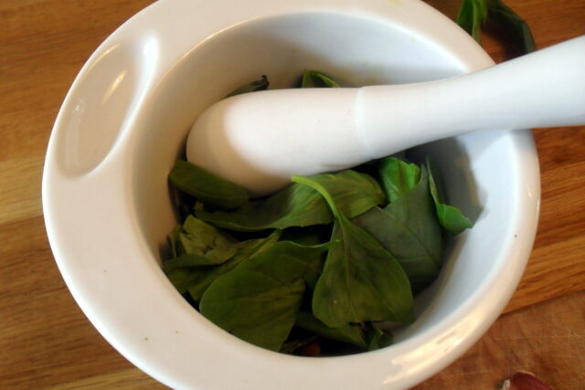 Preparazione pesto di basilico light: aggiunta delle prime foglie di basilico fresco nel mortaio