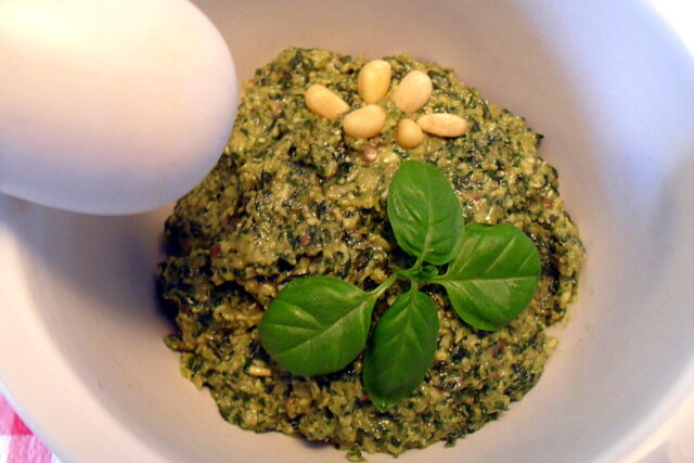 Preparazione pesto di basilico light: pesto pronto nel mortaio decorato con pinoli a fiore e ciuffo di basilico