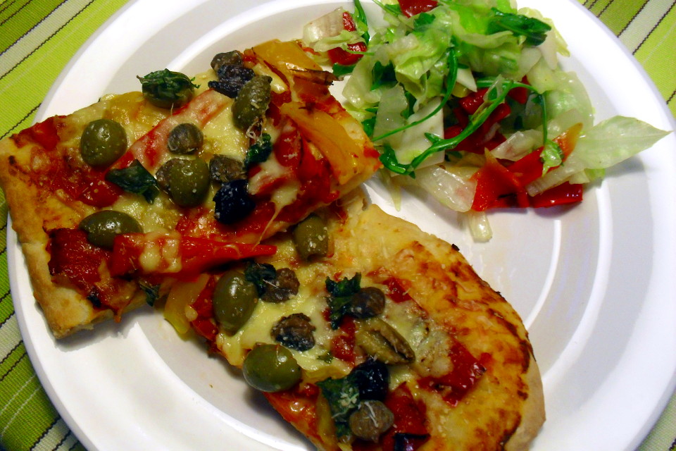 Pizza peperoni e olive light due tranci nel piatto con contorno di insalata fresca