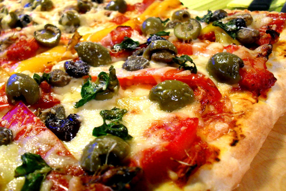 Preparazione pizza peperoni e olive light: inquadratura ravvicinata del trancio di pizza condito prima del taglio