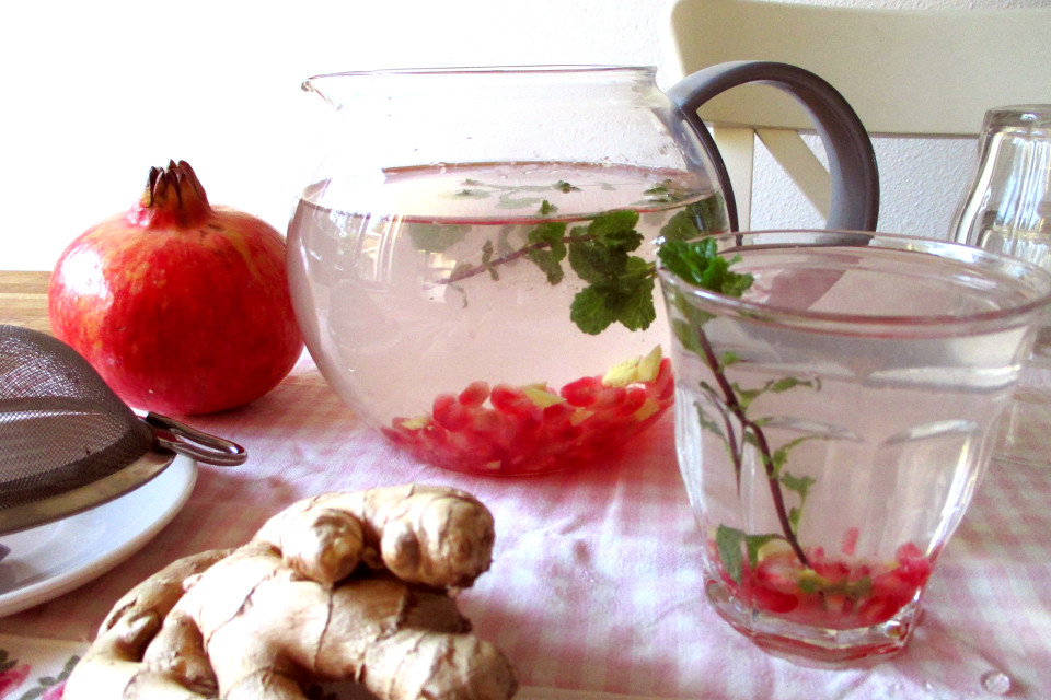Bevanda depurativa melagrana, zenzero e menta in una brocca di vetro e in un bicchiere, con melagrana e radice di zenzero accanto