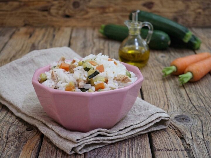 Una ciotola rosa piena di insalta di riso con petto di pollo, carote e zucchine a dadini