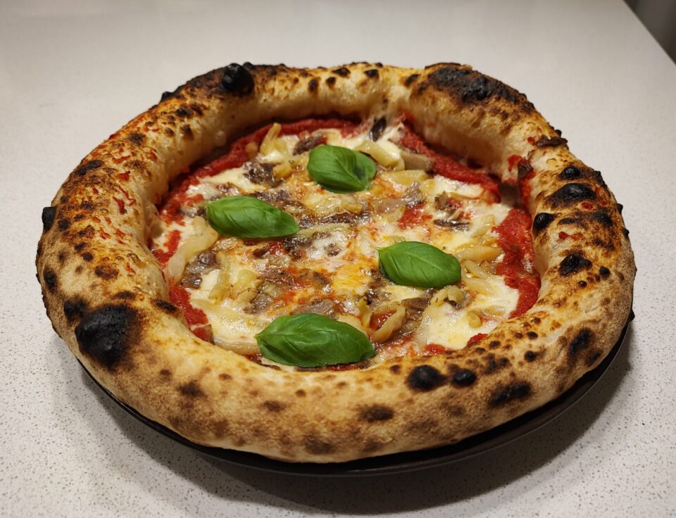 Pizza napoletana contemporanea vista frontalmente, con topping di pomodoro, fior di latte, cicoli napoletani, melanzane sott'olio e basilico fresco