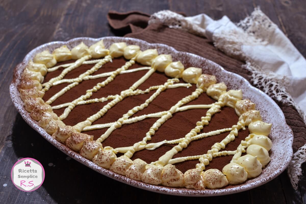 Tiramisù senza savoiardi con mascarpone, servito su un piatto ovale, decorato con cacao amaro e una raffinata grata di crema.