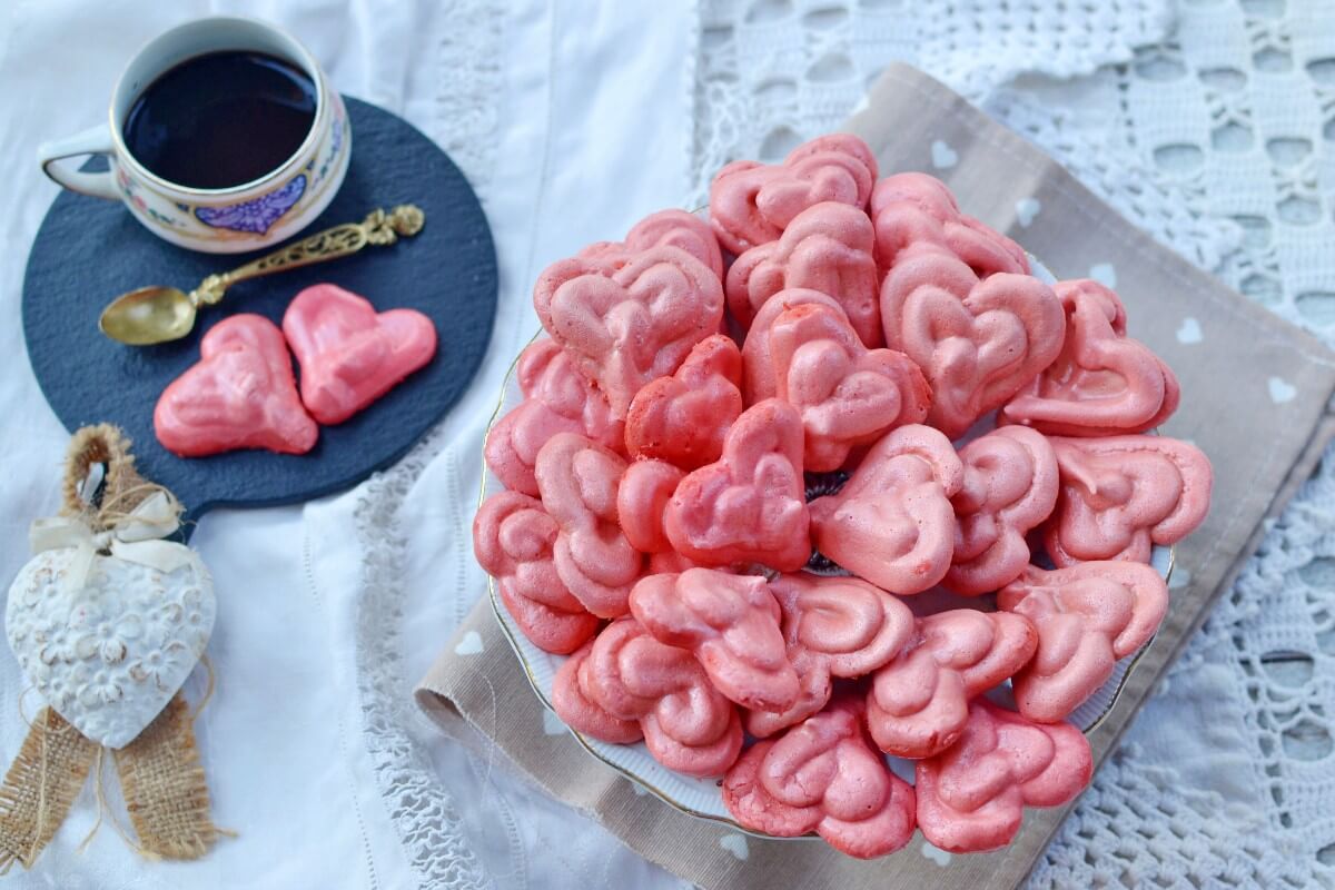 Biscotti di meringa a cuore rosa su tavola elegante, vista dall’alto