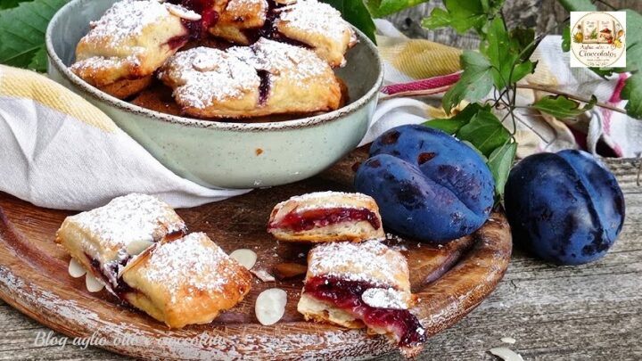 Biscotti di frolla all'acqua dorati ripieni di marmellata e mandorle a lamelle su tagliere di legno rustico