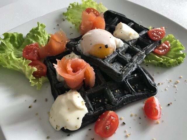 Waffle salati con farina nera, uovo in camicia, salmone affumicato e stracchino
